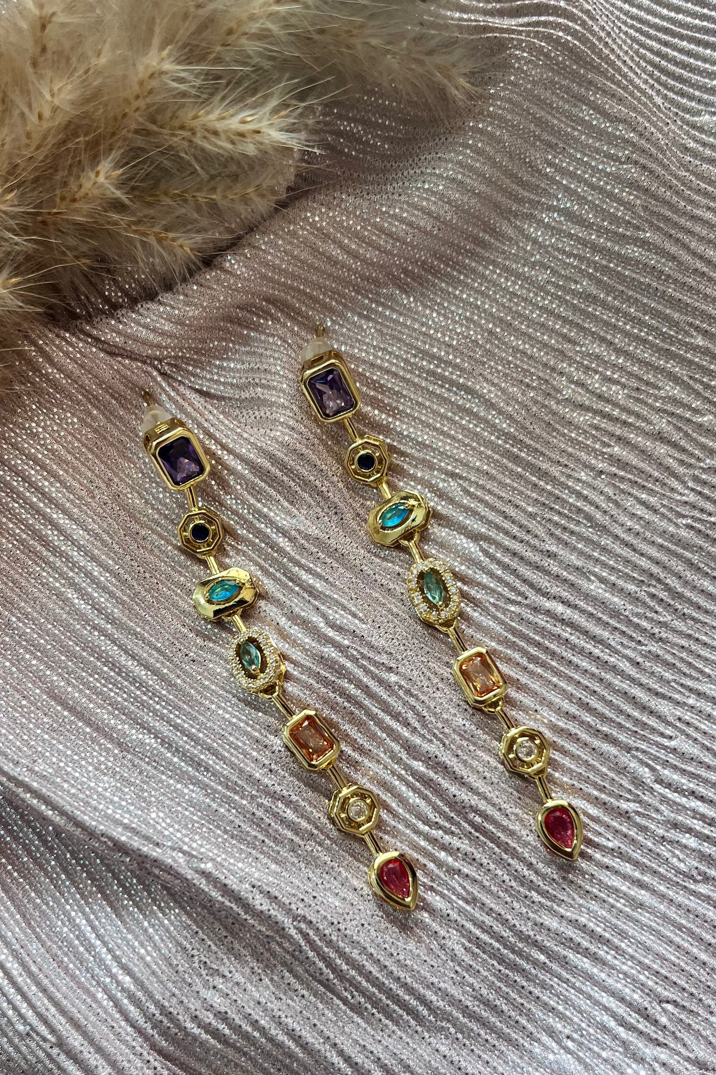 Gold earrings with gemstones on a textured fabric background