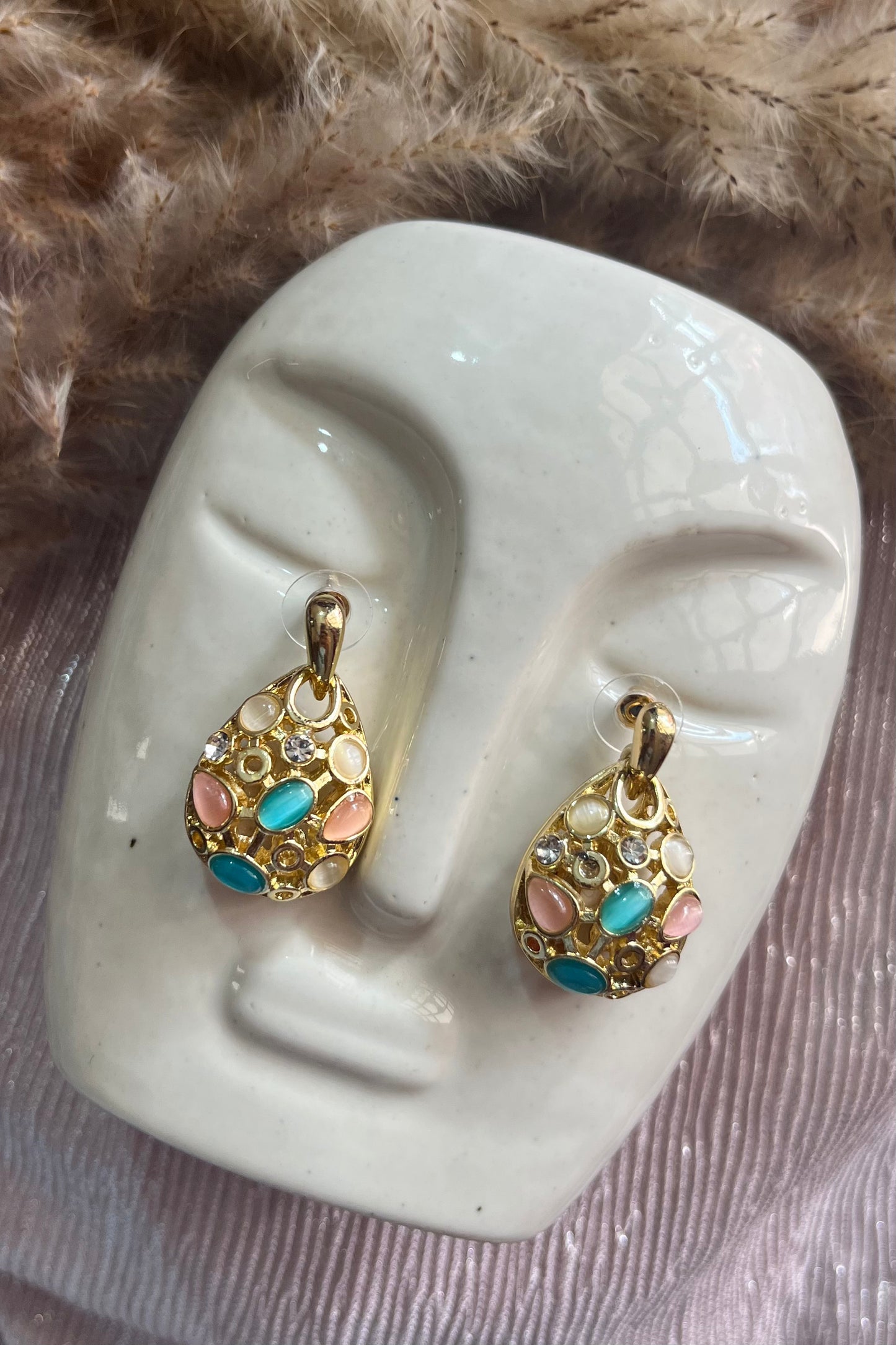 Gold earrings with colorful stones on a mannequin ear against a fur background